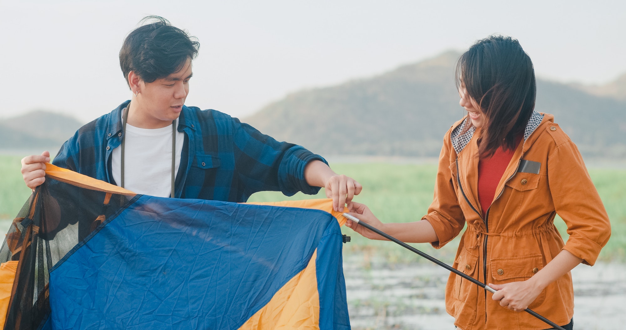 Young asia campers couple setting up the tent camping gear outdoor near seaside.